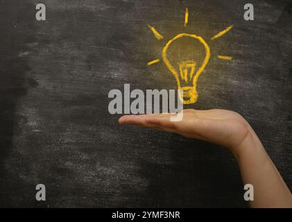 Mano che regge una lavagna con sopra una lampadina. La lampadina è gialla e presenta un contorno bianco. Concetto di creatività e innovazione Foto Stock