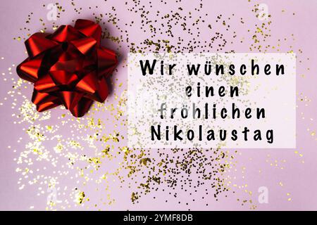 Fiocco rosso su un tavolo con glitter dorato. L'arco è avvolto intorno a un dono e le parole Wir wunschen einen frohlichen Nikolaufstag sono scritte sotto i Foto Stock