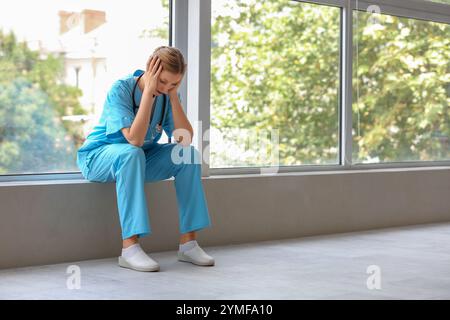 Medico stanco con stetoscopio seduto vicino alla finestra in clinica Foto Stock