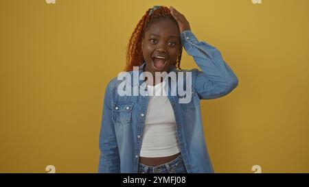 Una giovane donna afroamericana esprime sorpresa con un abbigliamento casual in denim su un vivace sfondo giallo. Foto Stock