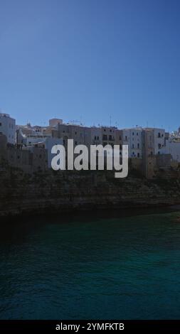 Vista panoramica della città costiera di polignano a mare in puglia, italia, con le sue affascinanti case sulla scogliera contro un cielo azzurro e limpido sopra l'adri Foto Stock