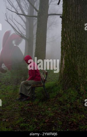 Una donna triste su una panchina del parco nella nebbia. Un drago che la guarda. Foto Stock