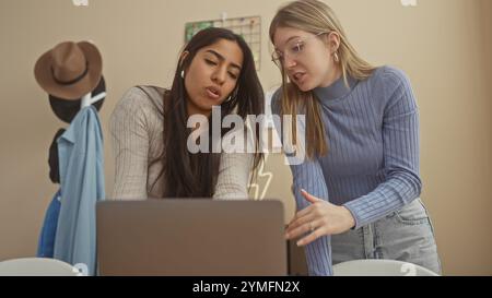 Due donne che collaborano a un progetto in un accogliente appartamento con una che punta sullo schermo di un laptop. Foto Stock