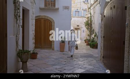 La giovane donna ispanica cammina attraverso le affascinanti stradine di polignano a mare, puglia, italia, mostrando una splendida architettura storica e vivace Foto Stock