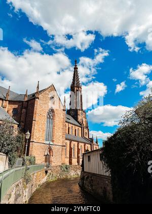 Una chiesa con un alto campanile e un cielo blu. Il cielo è parzialmente nuvoloso. La chiesa è circondata da un muro di mattoni Foto Stock