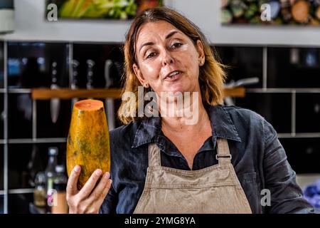 Helmi Smeulders tiene una papaya a fette (carica papaya) con polpa arancione nella sua scuola di cucina a Djonora Marthaweg, Willemstad, Curaceo. I semi neri della papaia hanno un sapore piccante e piccante che ricorda il rafano e vengono essiccati da Smeulders per essere utilizzati come spezie da cucina. Kòrsou Foto Stock