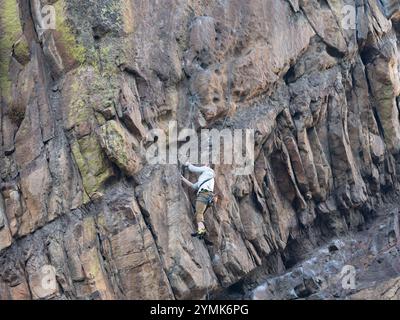 Un solo uomo arrampicatore che indossa l'imbracatura di sicurezza usando una fessura per le dita sulla Bastille Mountain nell'Eldorado Canyon State Park in Colorado. Foto Stock