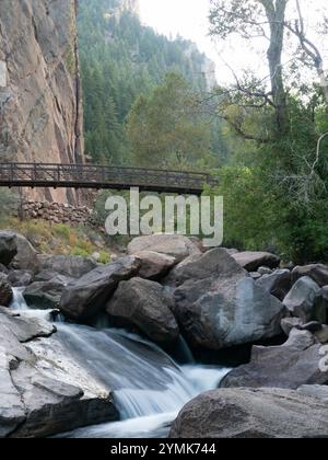 Vista ad angolo basso di una piccola cascata nel South Boulder Creek e della Bastiglia e di una passerella sullo sfondo. Fotografato in Eldorado Canyon St Foto Stock