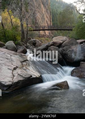 Vista ad angolo basso di una cascata nel South Boulder Creek e della Bastiglia e di una passerella sullo sfondo. Fotografato nell'Eldorado Canyon State Pa Foto Stock