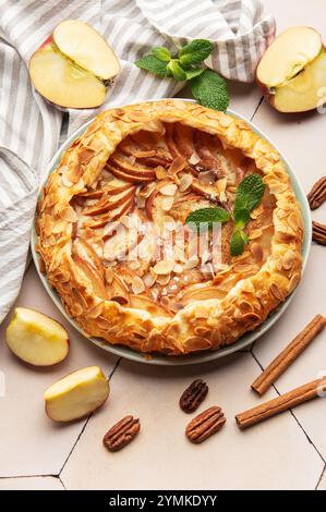 galette di mele appena sfornata decorata con fiocchi di mandorle, foglie di menta e bastoncini di cannella, incarnando la bontà fatta in casa Foto Stock