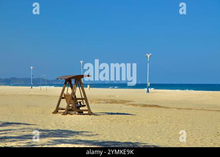 Contea di Yangyang, Corea del Sud - 3 novembre 2024: Un'altalena di legno poggia sulla distesa sabbiosa di Hajodae Beach, con il Mare Orientale e il lontano skyline della città Foto Stock