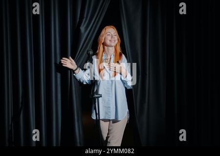 Donna sorridente in piedi dietro le tende Black Stage Foto Stock