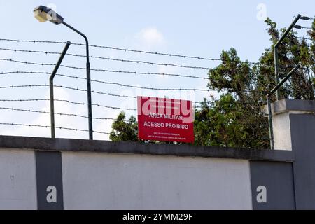 Filo spinato che ricopre una parete perimetrale con un cartello di divieto di violazione che protegge un'area militare limitata Foto Stock