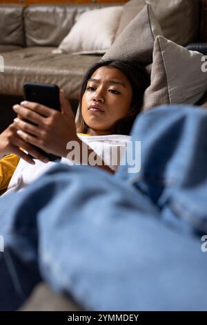 Adolescente asiatica che si rilassa sul divano, concentrata sullo smartphone a casa. tecnologia, relax, vacanza, tempo libero, gioventù, soggiorno Foto Stock