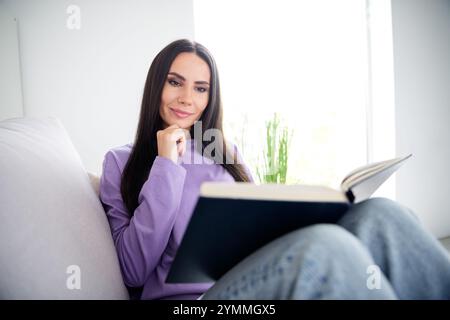 Una giovane donna in un elegante pullover gode di una lettura tranquilla in un accogliente appartamento Foto Stock