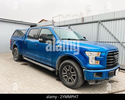 Kiev, Ucraina - 22 novembre 2024: Pick-up blu Ford F 150 con cabina estesa parcheggiata su una superficie pavimentata accanto a una recinzione metallica. Ideale per un Foto Stock