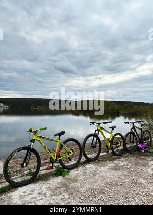 Kiev, Ucraina - 22 novembre 2024: Tre mountain bike cinetiche sono allineate accanto a un tranquillo lago, che riflette il cielo coperto. Il paesaggio tranquillo Foto Stock