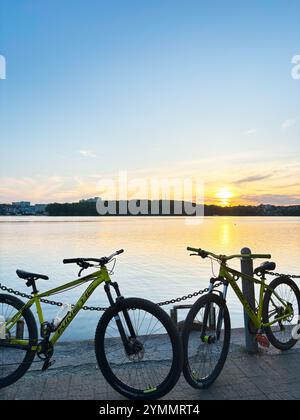 Kiev, Ucraina - 22 novembre 2024: Due biciclette cinetiche sono parcheggiate da un tranquillo lungolago, che cattura un tranquillo tramonto. L'acqua calma e il cielo vibrante c Foto Stock