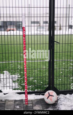 Pallone da calcio appoggiato a un bastone di zucchero vicino a un campo recintato, che mescola lo spirito natalizio con lo sport in un ambiente innevato. Foto Stock