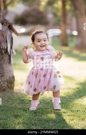 Bambino che cammina verso la macchina fotografica con un abito rosa di fragole Foto Stock