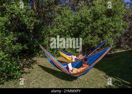 Due fratelli che si rilassano sulle amache con i libri Foto Stock