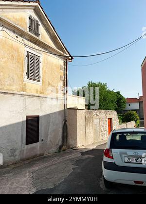 Zara, Croazia - 14 novembre 2024: Una strada tranquilla caratterizzata da un vecchio edificio con un'auto bianca parcheggiata. La scena cattura una fetta di rustico Foto Stock