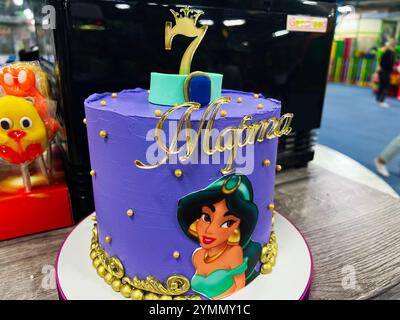 Kiev, Ucraina - 22 novembre 2024: Una colorata torta Jasmine di compleanno adornata da un personaggio di principessa dei cartoni animati, elegante scritta in oro e un numero se Foto Stock