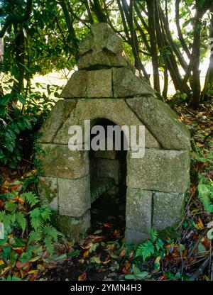 Vista SSW di St Cuby's Well, Duloe, Cornovaglia, Inghilterra, Regno Unito, mostra la casa del pozzo esterno con una panchina di pietra che fronteggia la più antica camera del pozzo. Foto Stock