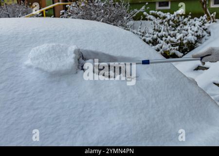 Una donna spara la neve dalla macchina, rimuovendo il ghiaccio dal corpo della macchina, attaccando l'inverno, preparando la macchina per il percorso Foto Stock