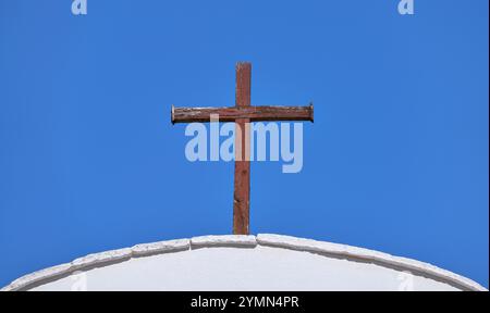 Antica croce cristiana realizzata in legno marrone intemprato su un tetto ad arco bianco Foto Stock