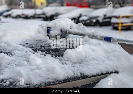 Una donna spara la neve dalla macchina, rimuovendo il ghiaccio dal corpo della macchina, attaccando l'inverno, preparando la macchina per il percorso Foto Stock