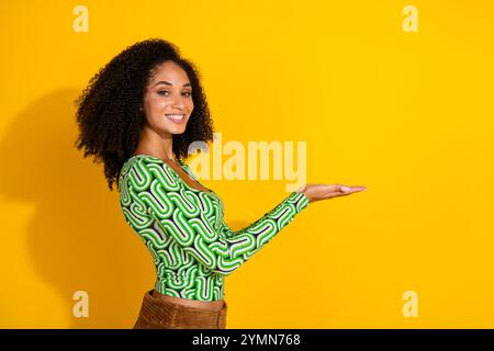 Giovane donna con capelli ricci nella parte superiore verde su sfondo giallo che presenta uno spazio vuoto Foto Stock
