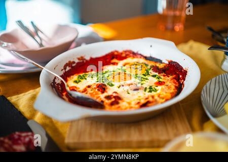 Stuzzicante shakshuka con uova ben preparate in camicia in una ricca salsa di pomodoro, guarnita con erbe aromatiche, su un tavolo da colazione. Ideale per una colazione abbondante Foto Stock