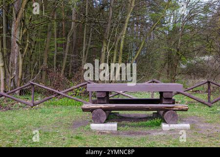 Banco in legno di tronchi sullo sfondo della foresta. Area ricreativa vicino alla foresta. Foto Stock