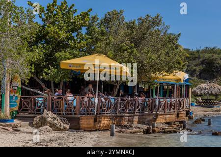 Il ristorante Brisa do Mar sulla spiaggia di Caracasbaaiweg, Jan Thiel, CuraCao, con una terrazza in legno proprio accanto all'acqua. Gli ombrelloni gialli recanti lo slogan «Born in CuraCao» fanno parte di una campagna pubblicitaria per il marchio di birra locale Brasa; questo popolare luogo di escursioni giornaliere si trova a circa dieci chilometri a est del centro di Willemstad. Kòrsou Foto Stock