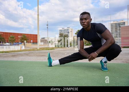 Giovane uomo nero che si allunga le gambe dopo un allenamento calistenico all'aperto Foto Stock