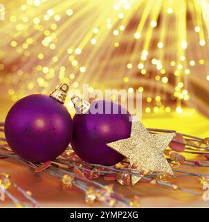 Decorazione di Capodanno su sfondo di luci gialle. Palline viola e una stella d'oro. Foto Stock