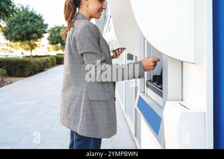 Donna d'affari in un elegante outfit casual che utilizza un bancomat in città. Foto Stock