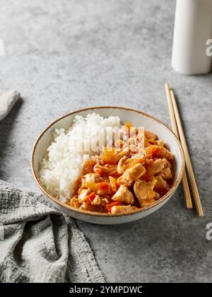ciotola di riso bollito con salsa agrodolce di pollo sul tavolo da cucina grigio Foto Stock