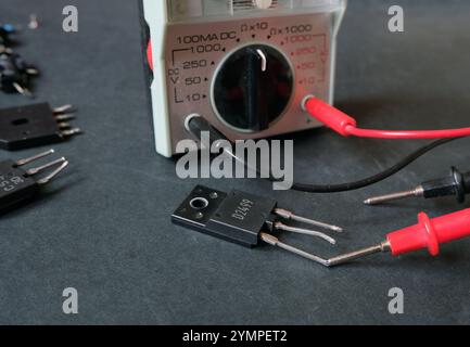 Un transistor di potenza sul banco con il multimetro. Focalizzata sul componente sottoposto a test. Foto Stock