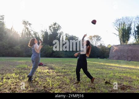 Due contadine si stanno godendo un momento di svago giocoso, gettando un cappello tra di loro nella luce dorata del tramonto Foto Stock