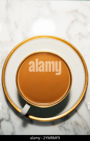 vista dall'alto del tè lattiginoso, caffè in tazza panna con piattino sul tavolo di marmo con spazio per le copie Foto Stock