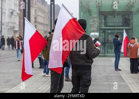 Persone che tengono bandiere polacche durante un tranquillo raduno pubblico in una piazza della città con edifici moderni e storici sullo sfondo Foto Stock