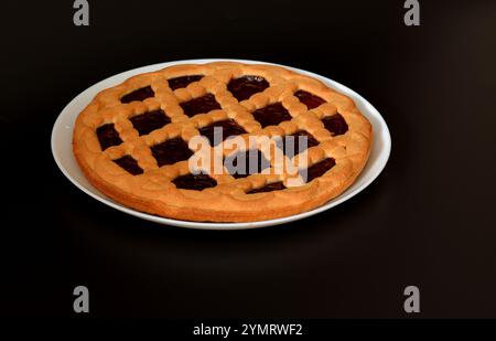 Ampia piastra rotonda in ceramica bianca con torta di ciliegie su sfondo nero. Primo piano. Foto Stock