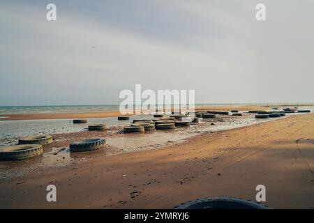 demolitori a onde realizzati con pneumatici usati posizionati lungo la spiaggia Foto Stock