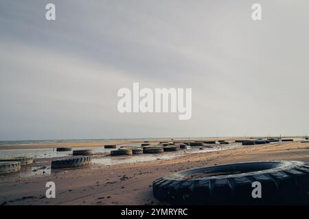 demolitori a onde realizzati con pneumatici usati posizionati lungo la spiaggia Foto Stock