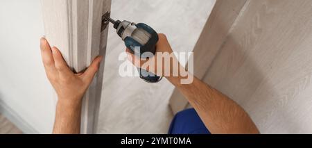 Lavoratore maschio con trapano elettrico che installa la piastra di battuta della porta a casa Foto Stock