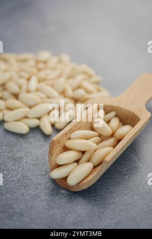 Cucchiaio in legno ripieno di noci di pino crudi freschi su sfondo grigio Foto Stock