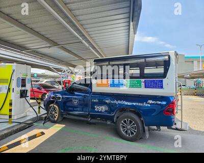 Pattaya Tailandia 17 novembre 2024, un vibrante camion taxi Songthaew blu si riempie in una stazione di ricarica elettrica sotto il sole luminoso. Foto Stock