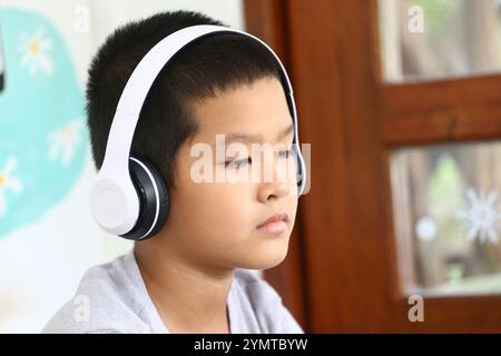 Un ragazzo che indossa le cuffie bianche si siede in silenzio e si concentra sulla sua musica. Questo momento sereno cattura l'essenza dell'innocenza infantile e del tempo libero. Foto Stock